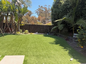 Un jardin avec une pelouse artificielle, une clôture en bois et diverses plantes.