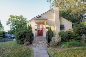 A two-story house with a red door, stone steps, and a brick chimney.