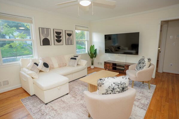 A modern living room with a white sofa, a coffee table, a TV, and a large window.