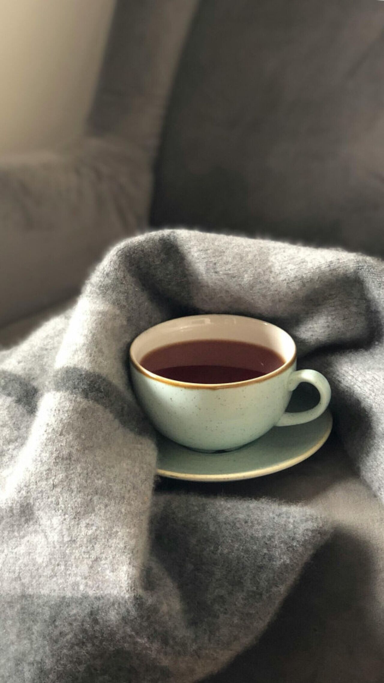 A cup of tea on a saucer placed on a textured grey blanket.