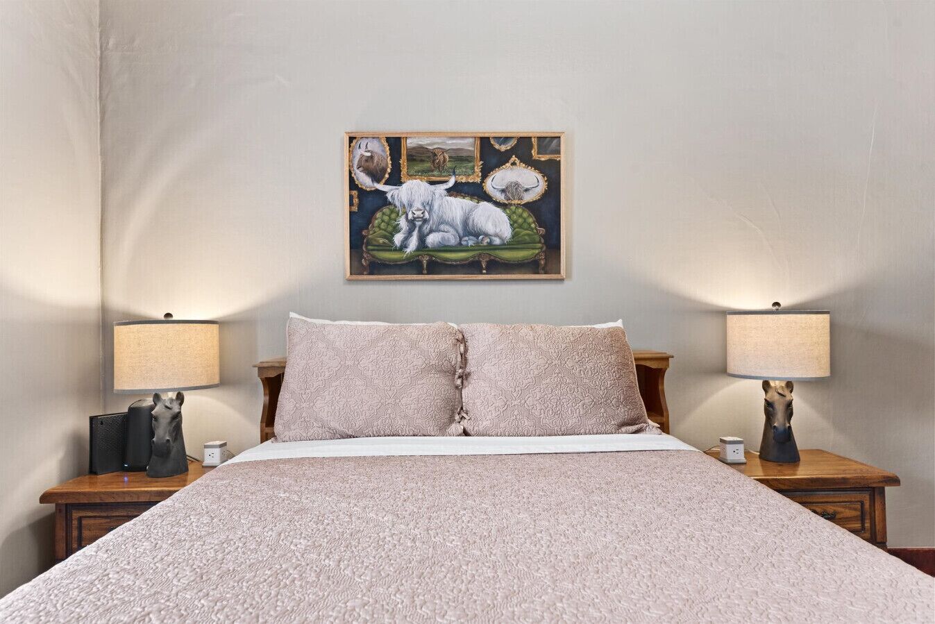 A bedroom with a large bed, two bedside tables, lamps, a framed picture, and a carpeted floor.