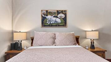 A bedroom with a large bed, two bedside tables, lamps, a framed picture, and a carpeted floor.