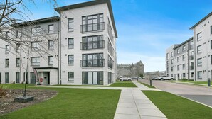 Un immeuble d’appartements moderne doté d’une cour intérieure, d’un chemin piétonnier pavé et offrant une vue sur un ciel dégagé.