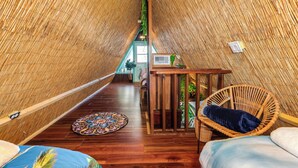 Ein Zimmer mit hoher Decke, Holzboden, einem Korbstuhl, einem kleinen Tisch und einem Bett mit blauer und weißer Bettdecke.