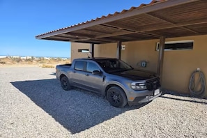 A silver pickup truck parked under a covered area with a gravel ground.