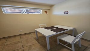 A small room with a white table and two chairs, a window with blinds, a wall-mounted light, and a small decorative item. - Casita Sol en el Dorado Rach para parejas/Starlink Wifi/Spa (B.C.)