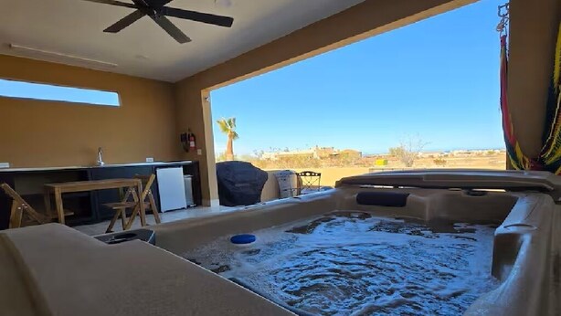 A hot tub with a view of a desert landscape, a ceiling fan, and a small kitchen area. - Casita Sol en el Dorado Rach para parejas/Starlink Wifi/Spa (B.C.)