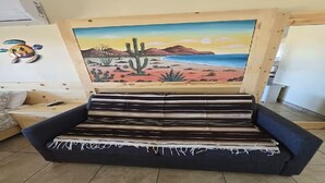 A sofa with a striped cushion, a painting of a desert landscape, and a turtle decoration on the wall. - Casita Sol en el Dorado Rach para parejas/Starlink Wifi/Spa (B.C.)
