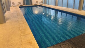 Een binnenzwembad met helder water, betegelde vloer en loungestoelen langs de randen.
