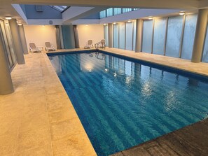 An indoor swimming pool with clear water, tiled flooring, and lounge chairs along the sides. - Península Frente al Mar, Piscina, Gym, 4 TVs, Parking, Patio y Jardín Privados (Punta De Este)