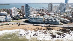 Paisatge urbà costaner amb edificis moderns alts, una platja i una riba rocosa.