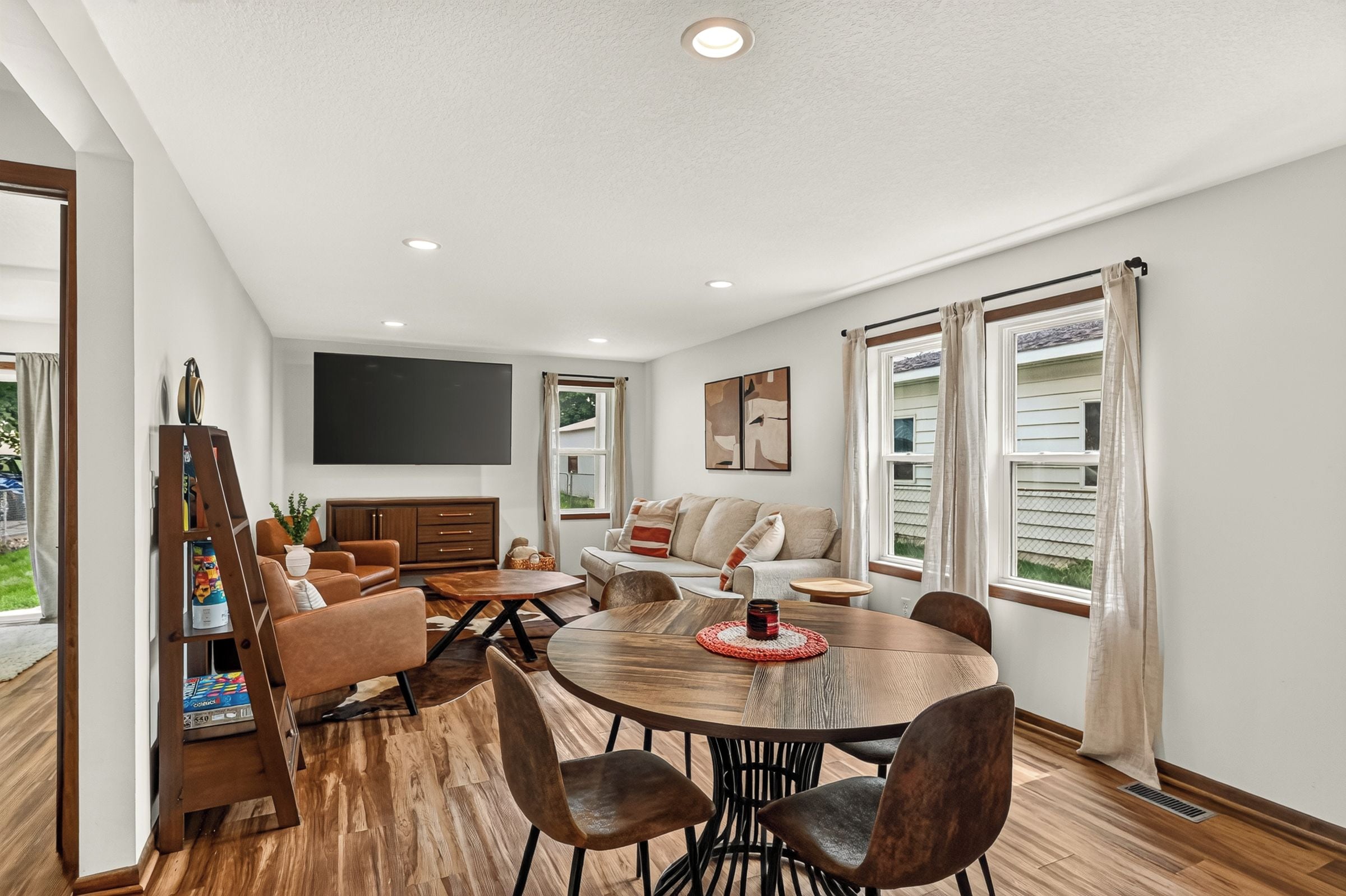 A spacious living room with a wooden dining table, leather sofas, and a flat-screen TV mounted on the wall.