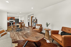 Un salon moderne avec un coin repas, une cuisine à l’arrière-plan et une vue sur le salon à travers une porte ouverte.