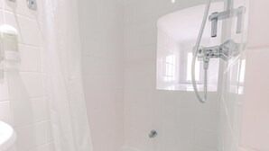 Un baño con azulejos blancos, ducha y ventana.