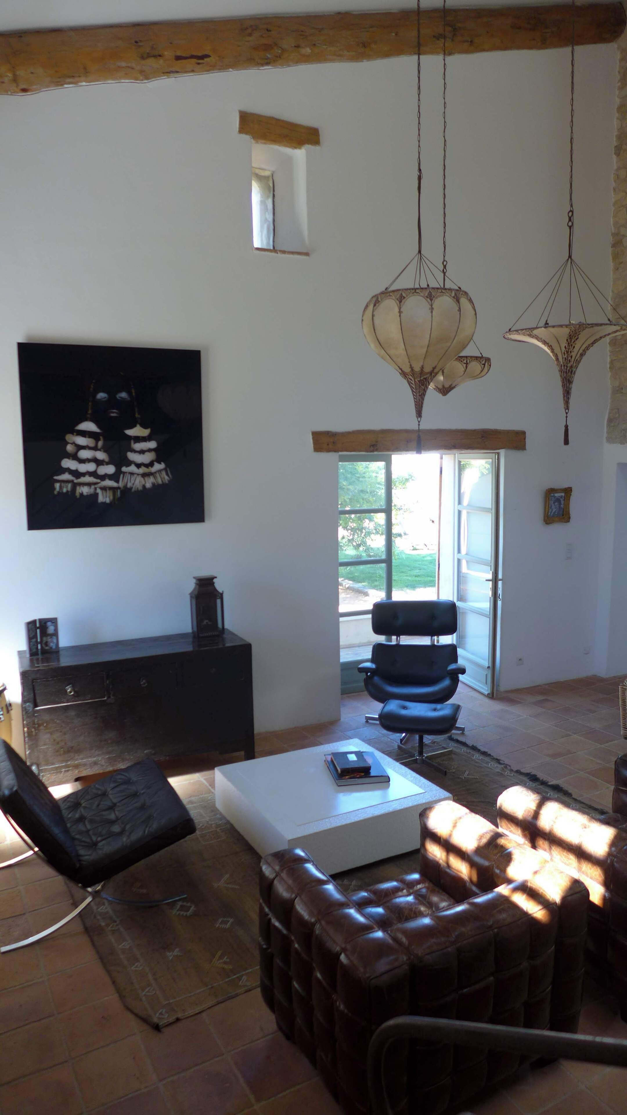 Un salon spacieux avec une grande fenêtre, un canapé noir, une table basse blanche et un luminaire suspendu.