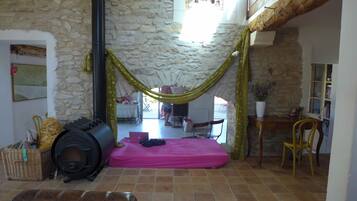 Une pièce avec un mur en pierre, un hamac, un lit, une cheminée et un bureau avec une chaise.