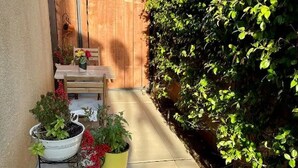 Un patio exterior estrecho con mesa y sillas de madera, plantas en macetas y cerca de madera.
