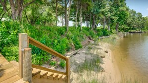 Un escalier en bois mène à la rive d’une rivière, bordée d’une végétation luxuriante et d’arbres.