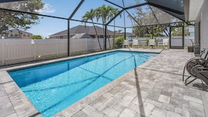 A swimming pool with a covered patio area, a white fence, and houses in the background. - New Enclosed Pool, Family Friendly Oasis (Cape Coral)