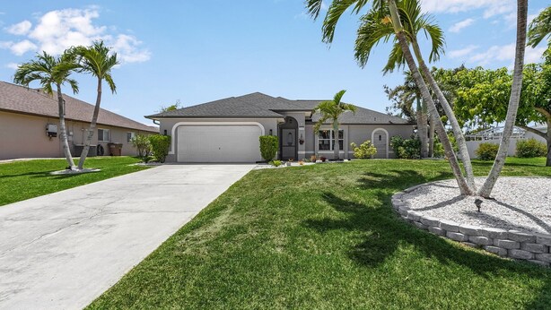A residential house with a driveway, lawn, and palm trees. - New Enclosed Pool, Family Friendly Oasis (Cape Coral)