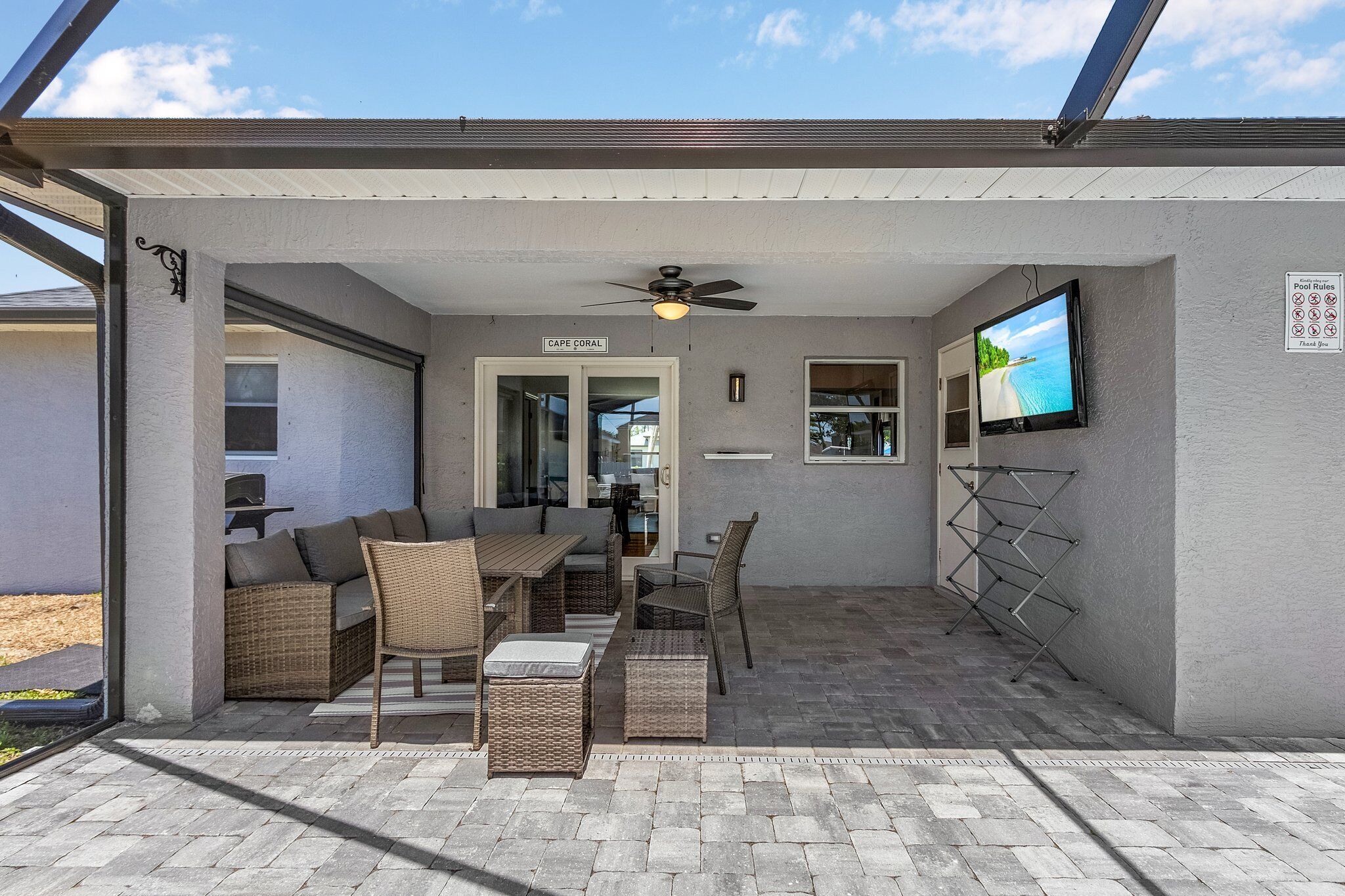 Ein überdachter Patio-Bereich mit Deckenventilator, einem an der Wand befestigten Fernseher und einem Schild mit Poolregeln.