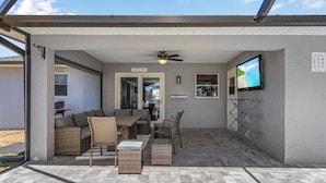 A covered patio area with a ceiling fan, a television mounted on the wall, and a sign indicating pool rules. - New Enclosed Pool, Family Friendly Oasis (Cape Coral)