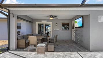 Ein überdachter Patio-Bereich mit Deckenventilator, einem an der Wand befestigten Fernseher und einem Schild mit Poolregeln.