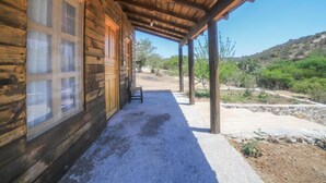 A wooden cabin with a covered porch, a gravel pathway, and a view of the surrounding landscape. - Centro de Aventuras Tatu (San Miguel de Allende)