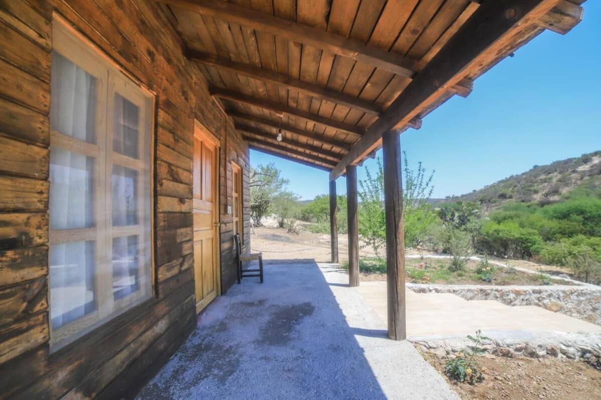 A wooden cabin with a covered porch, a gravel pathway, and a view of the surrounding landscape.