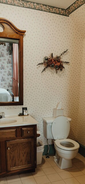 Une salle de bain avec un meuble-lavabo en bois, des toilettes blanches et un miroir orné d’un motif floral.