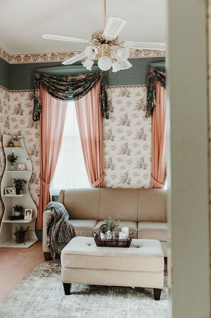 A cozy living room with a sofa, ottoman, and a decorative ceiling fan.