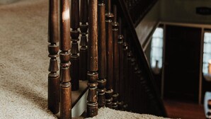 Eine hölzerne Treppe mit Handlauf, Teppichboden und Blick auf einen Raum mit Fenster und Vorhängen.