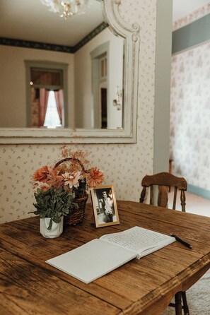 A wooden table with a vase of flowers, a framed photograph, and an open notebook with a pen.
