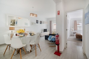 A modern living room with a dining area, a sofa, a TV, and a fire extinguisher. - Boat 4 Apt OCV – Near the Beach (100m) with Pool (Albufeira)