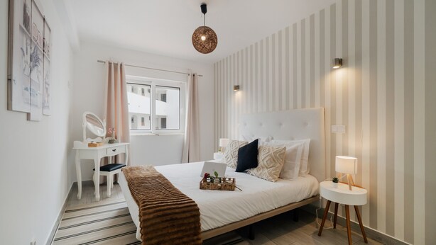 A bedroom with a bed, bedside table, lamp, desk, chair, and a window.