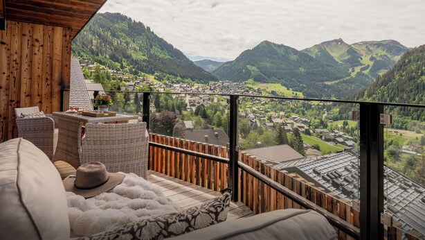 A balcony with a view of a mountainous landscape, wicker furniture, and a wooden ceiling.