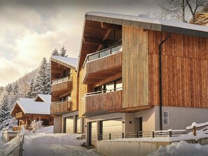 Un bâtiment moderne en bois, doté de balcons, d’une entrée couverte et surplombant un paysage enneigé.