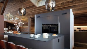 A modern kitchen with a central island, stainless steel appliances, and wooden ceiling beams.