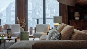 A cozy living room with a large window, wooden beams, and a view of snow-covered mountains.