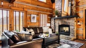 A log cabin interior with a stone fireplace, leather sofa, and large windows.