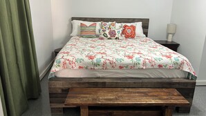 Una cama con cubrecama floral, cabecera de madera y un banco al pie de la cama.