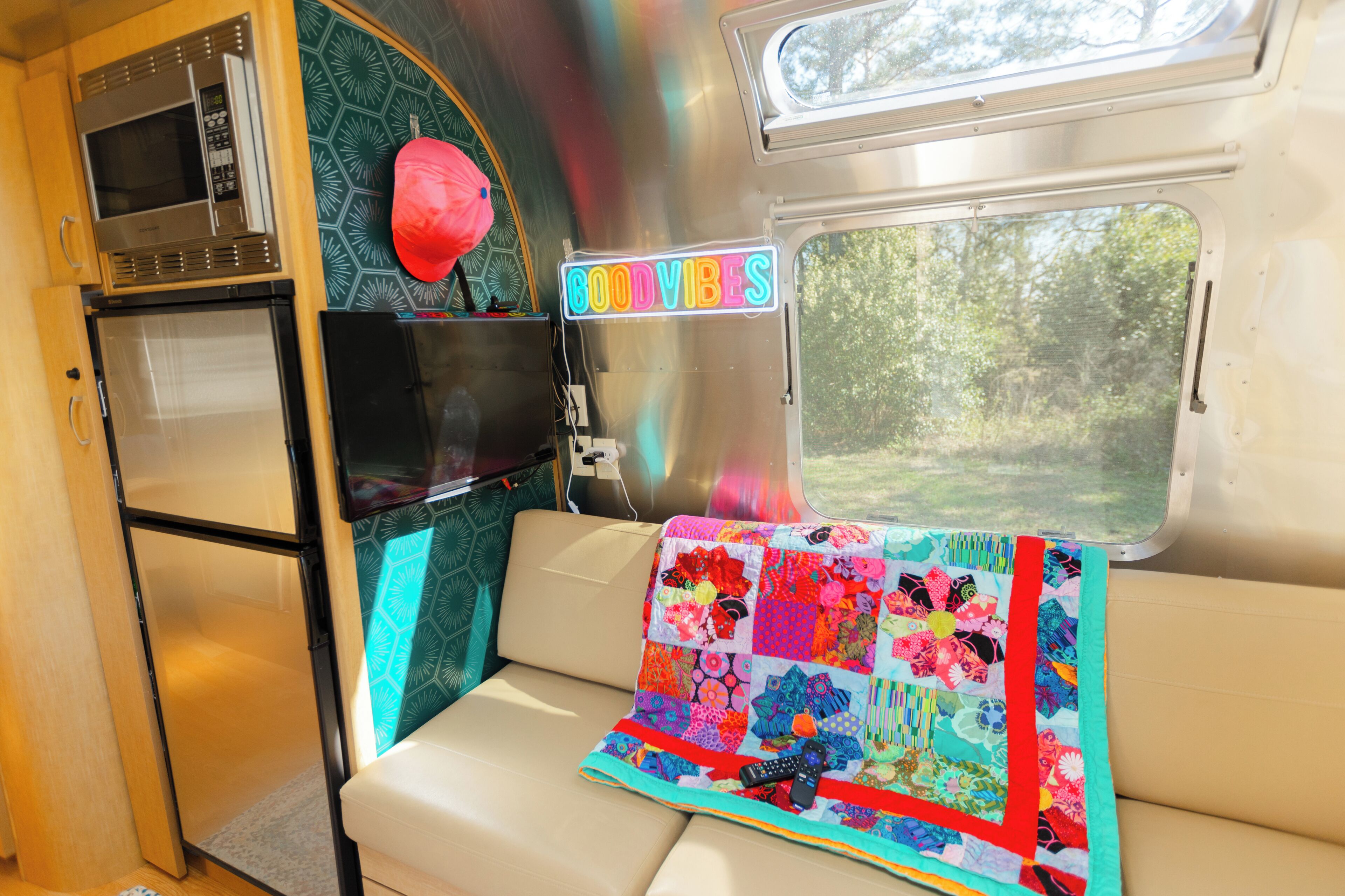 A cozy RV interior with a kitchenette, a quilted blanket, and a 'GOODVIBES' sign.
