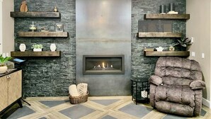 A living room with a fireplace, stone walls, and a plush armchair.