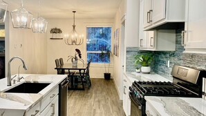 A modern kitchen with a central island, a dining area, and a view of the outdoors.