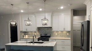 A modern kitchen with white cabinets, a central island with bar stools, stainless steel appliances, and pendant lighting.