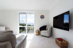A living room with a sofa, a patterned armchair, a flat-screen TV, a window with a view, and a wall-mounted picture. - Serene Trevallyn Escape & Views (Trevallyn)