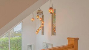 A staircase with a wooden handrail, a series of hanging decorative lights, and a wall with framed artwork. - Family Fun Home: Hot Tub, Arcade, Game Room | 6BR (Cardiff)