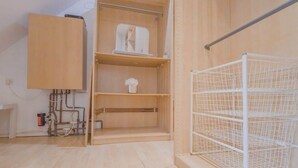 A room with a wooden wardrobe, a white metal shelf, and a white wire shelf unit. - Family Fun Home: Hot Tub, Arcade, Game Room | 6BR (Cardiff)
