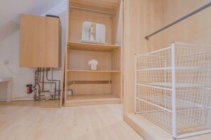 A room with a wooden wardrobe, a white metal shelf, and a white wire shelf unit. - Family Fun Home: Hot Tub, Arcade, Game Room | 6BR (Cardiff)