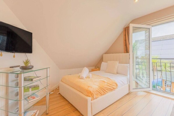 A bedroom with a bed, a glass table with books, a TV, and a balcony with a view.